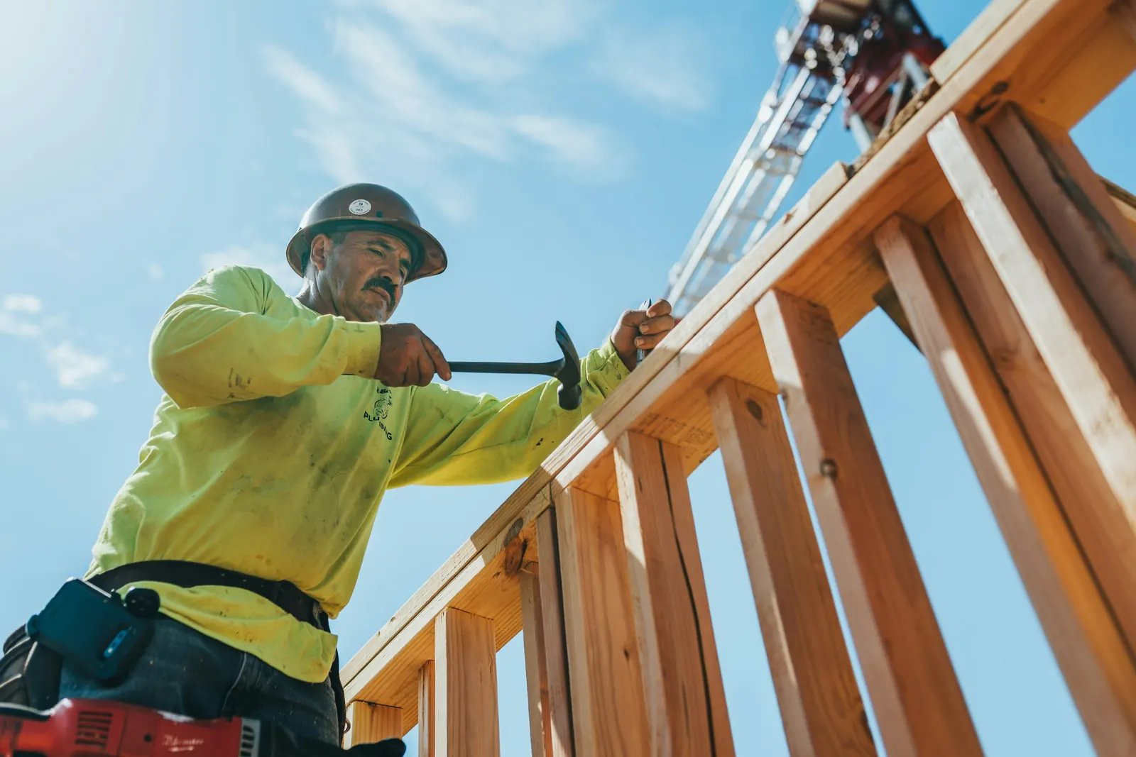 A builder in a hi-vis shirt nailing timber wall framing on a house under construction